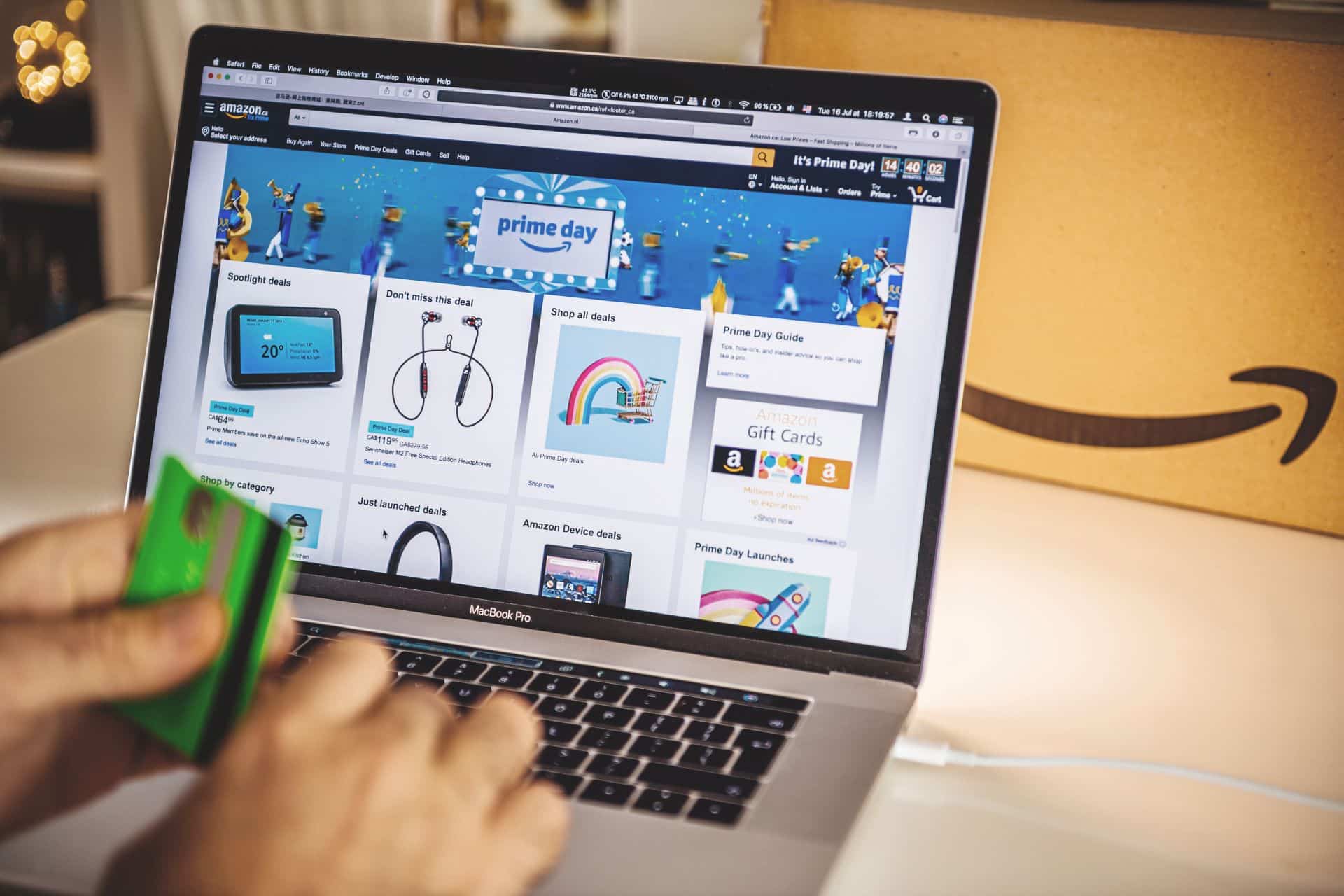 Person hält eine grüne Kreditkarte und nutzt einen Laptop, um auf der Amazon Prime Day-Seite zu shoppen. Der Bildschirm zeigt verschiedene Angebote und Deals auf Amazon.