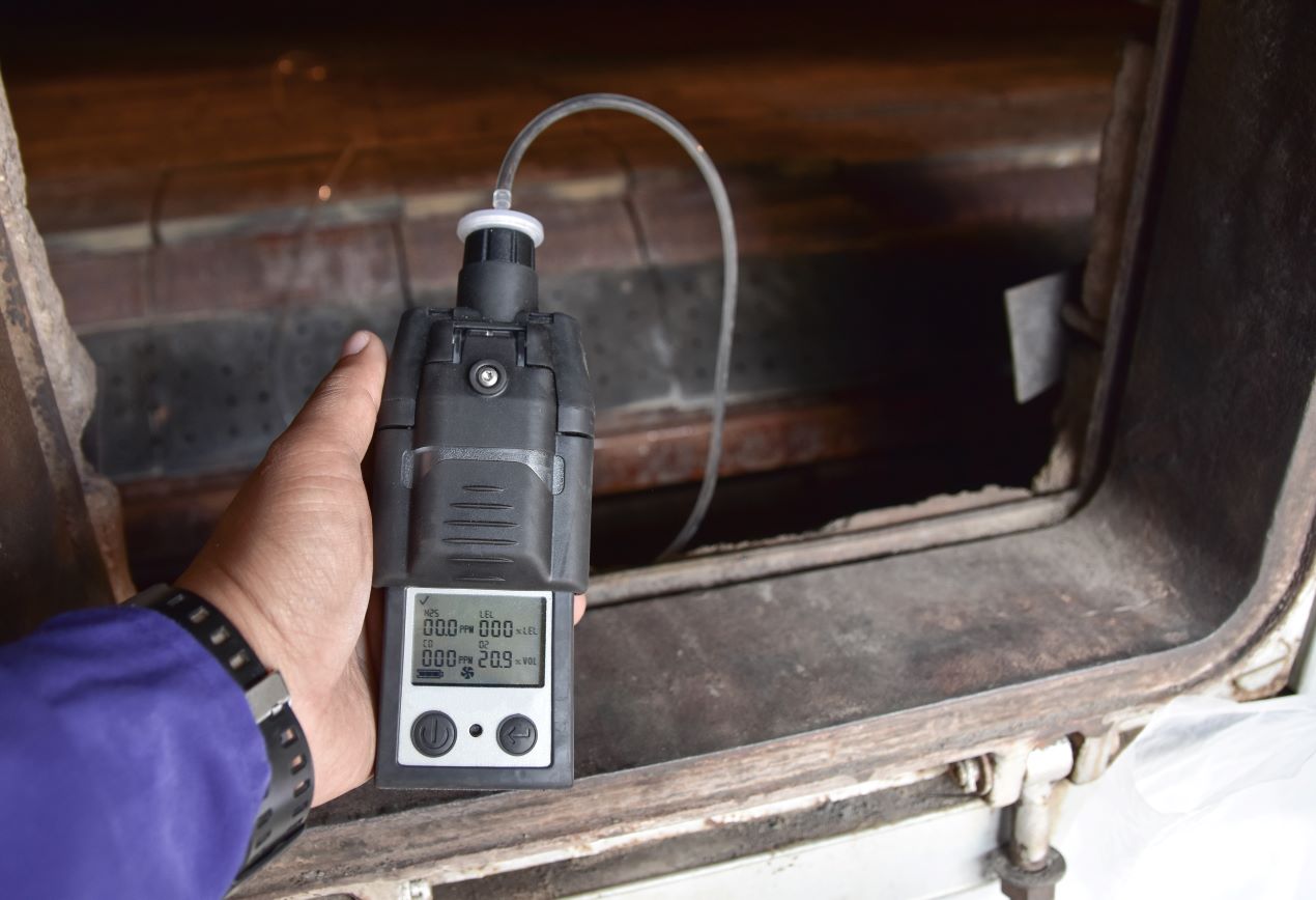 Close-up of a technician using a portable hydrogen sensor to detect gas leaks in an industrial setting