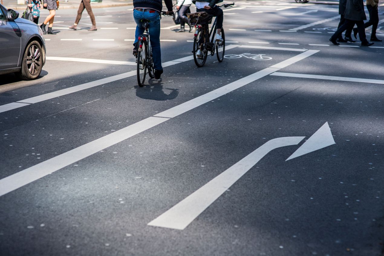 Fahrbahn Markierung mit weissen Richtungspfeilen und Fahrradweg auf innerstaedtischer Kreuzung bei Tageslicht