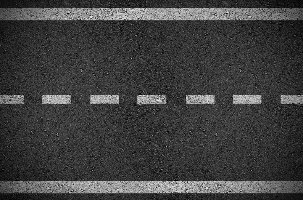 Fahrbahn Markierung mit weisser gestrichelter Linie auf dunklem Asphaltbelag in Nahaufnahme