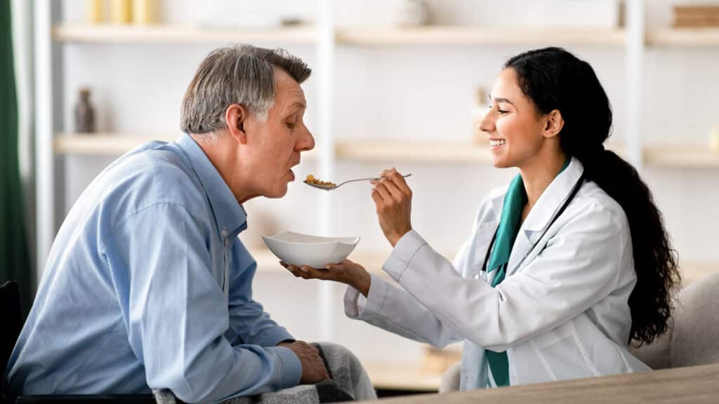 Pflegekraft unterstützt Senior beim Essen